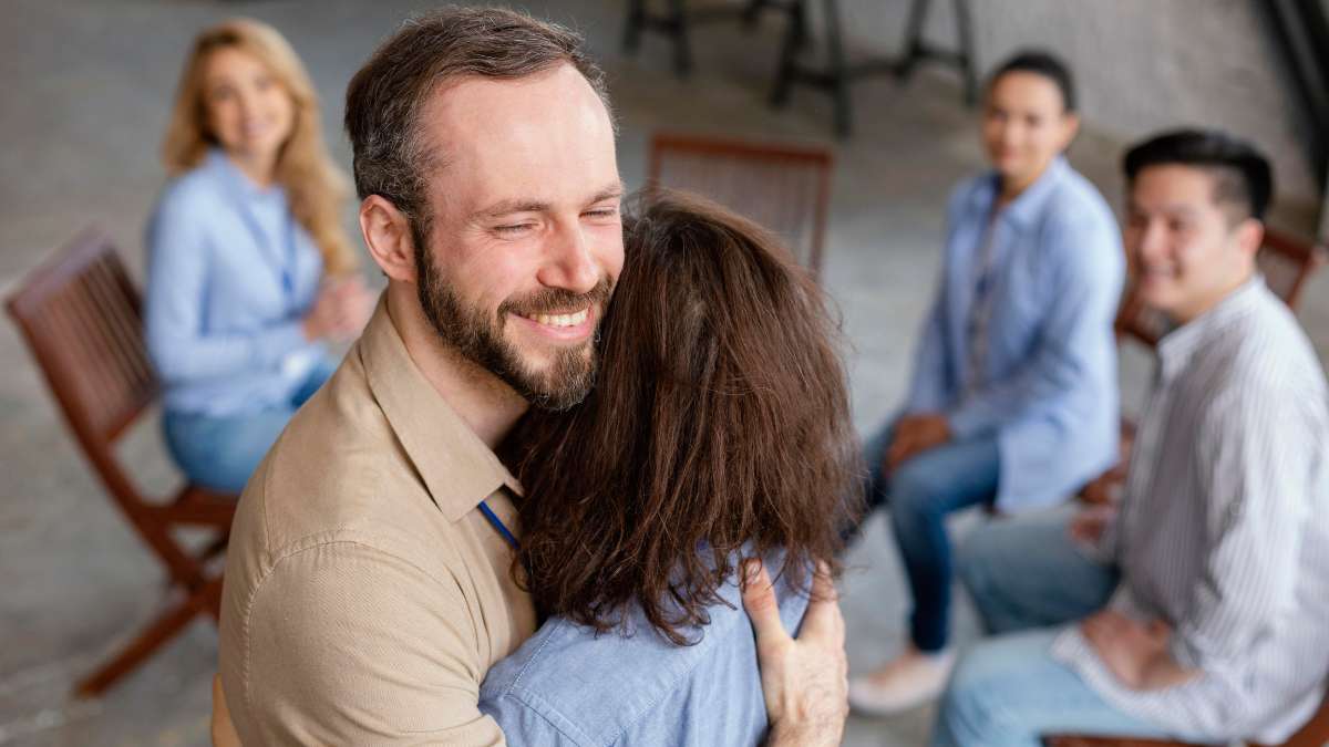 Group of people during community therapy as part of the drug detox program. Supportive therapist hugging female patient. 