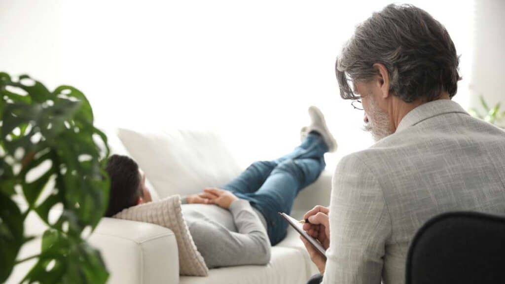 Male patient on sofa with healthcare specialist evaluating during heroin detox.